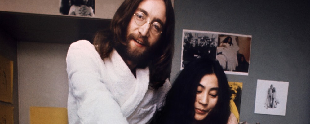 US musician John Lennon (R) and his japanese wife Yoko Ono (L) pose for photographers in pyjamas near a bicycle "Provo" in Amsterdam 27 March 1969. The honeymoon couple who was spending a week in bed at Hilton Hotel to protest against world violence had to leave the comfort of their bed to try out a Provo white bicycle which had been presented to them today. (FILM) AFP PHOTO (Photo credit should read -/AFP/Getty Images)